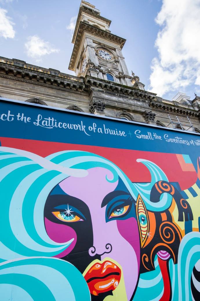 The Dunedin Municipal Chambers clocktower and the street art hoarding around its base.