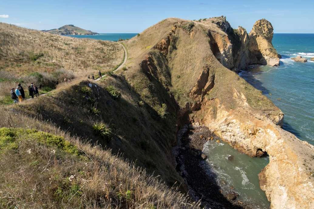 People walk the trail along the coastal Huriawa Peninsula past the blow hole.