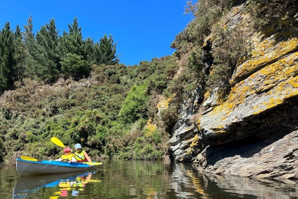 An adult and child in a kayak paddle on the creek.