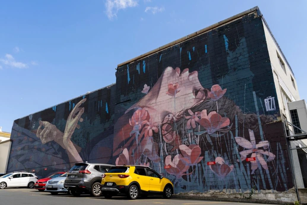 A mural in a carpark depicts a woman dying in a field of flowers.