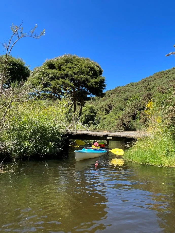 A kayaker lies flat and paddles under the bridge.